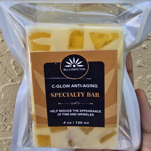 Packaged C-Glow Anti-Aging Specialty Soap with visible natural ingredients within the bar, held in a person's hand.